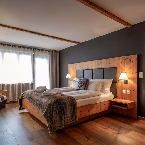 La Val Hotel & Spa: Ihr Hotel in Breil/Brigels Gemütliches Hotelzimmer mit Holzbett, Fernseher und Tageslicht durch Fenster