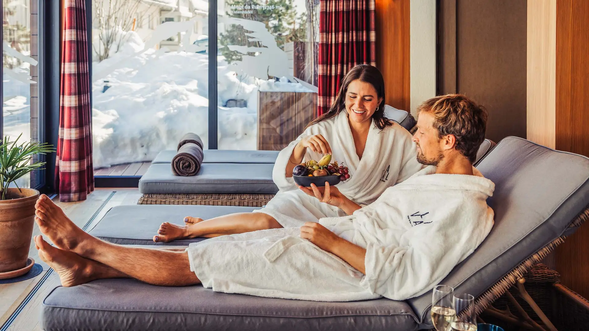 La Val Hotel & Spa: Ihr Hotel in Breil/Brigels Paar in Bademänteln entspannt auf Liegen mit Winterblick und Obstschale