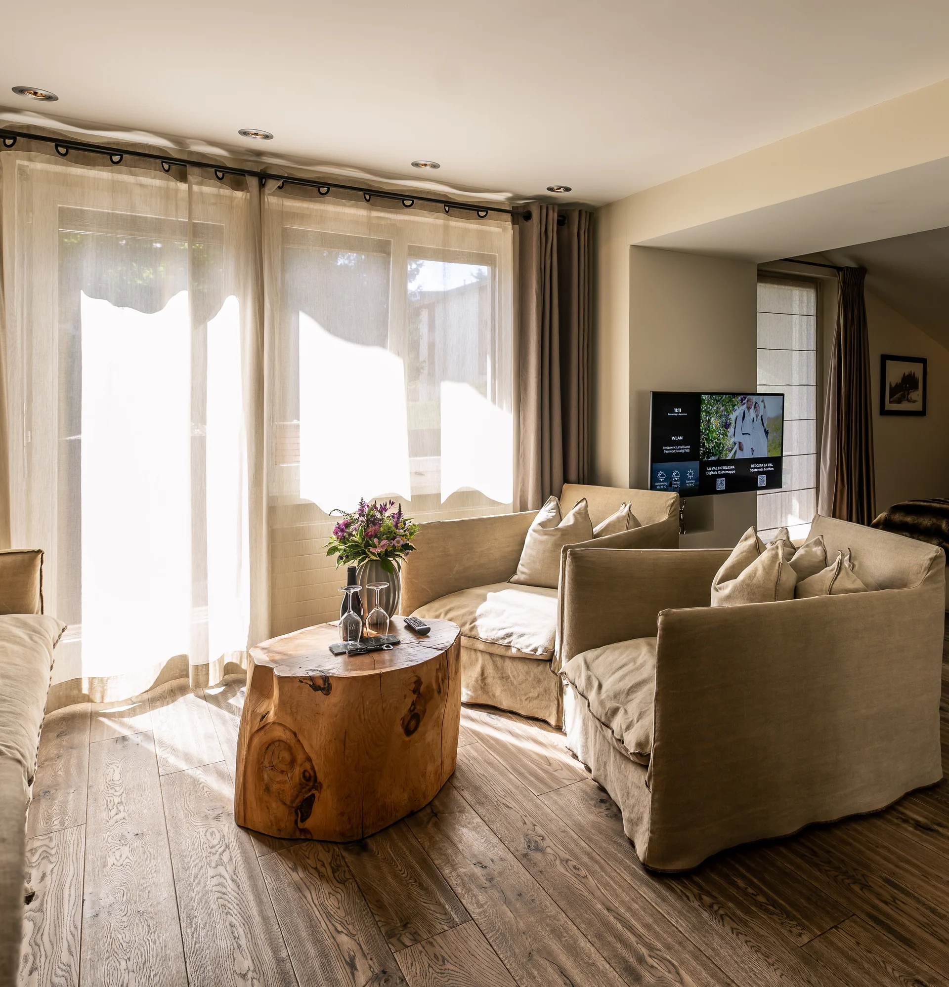 La Val Hotel & Spa: Ihr Hotel in Breil/Brigels Wohnbereich mit beige Sofas, Holz-Couchtisch und Blick ins Schlafzimmer