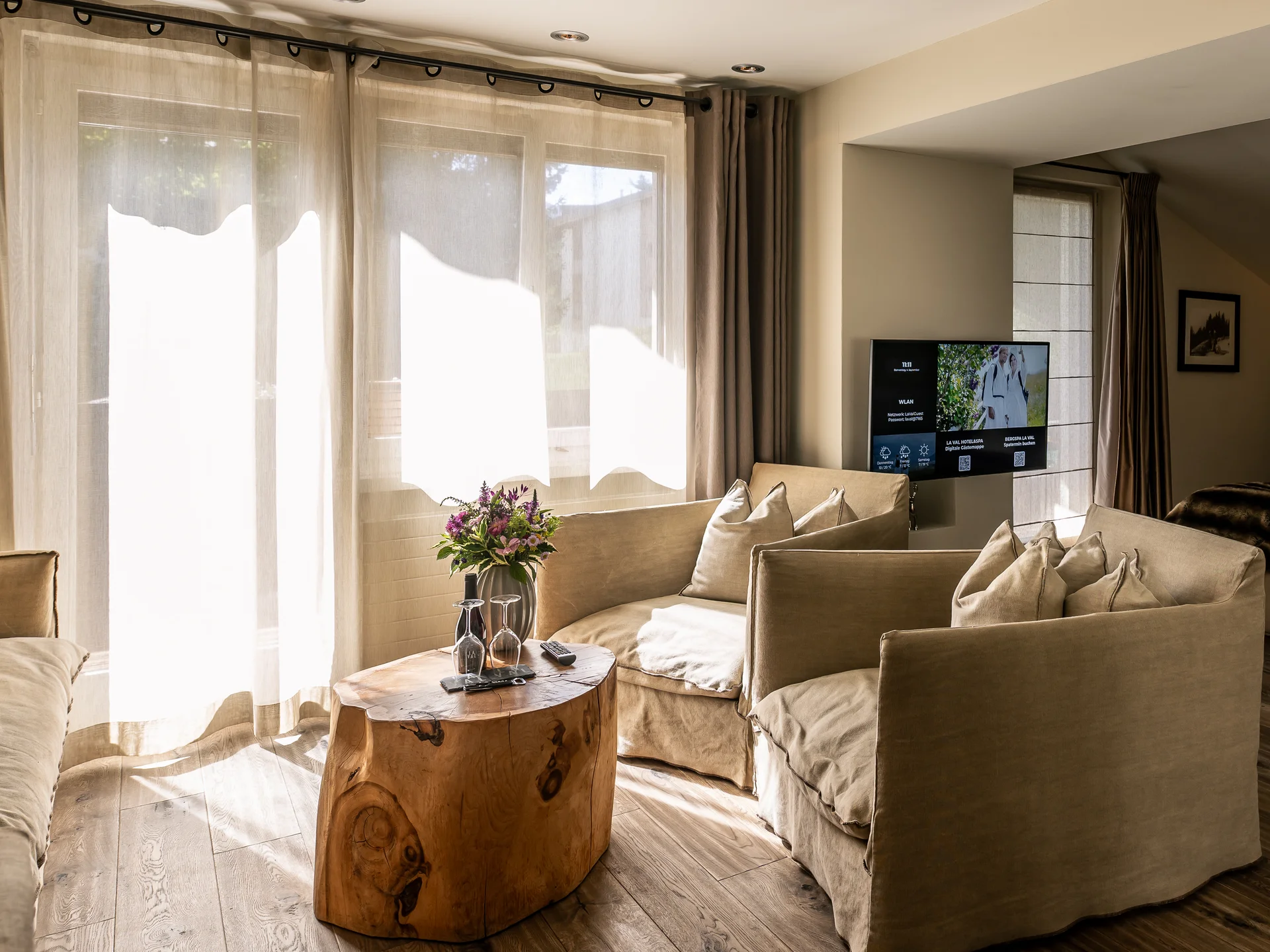 La Val Hotel & Spa: Ihr Hotel in Breil/Brigels Wohnbereich mit beige Sofas, Holz-Couchtisch und Blick ins Schlafzimmer