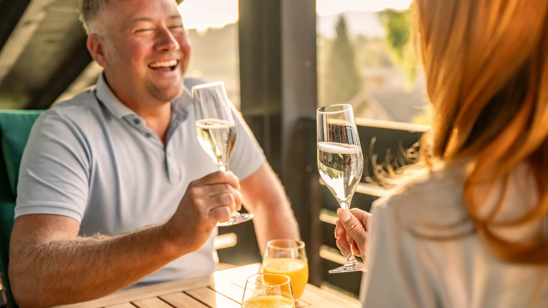 La Val Hotel & Spa: Ihr Hotel in Breil/Brigels Paar stößt mit Champagnergläsern auf einem Balkon an, Orangensaftgläser stehen auf dem Tisch