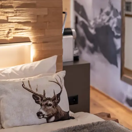 La Val Hotel & Spa: Ihr Hotel in Breil/Brigels Kissen mit Hirschmotiv auf einem Bett vor einem beleuchteten Holzpaneel