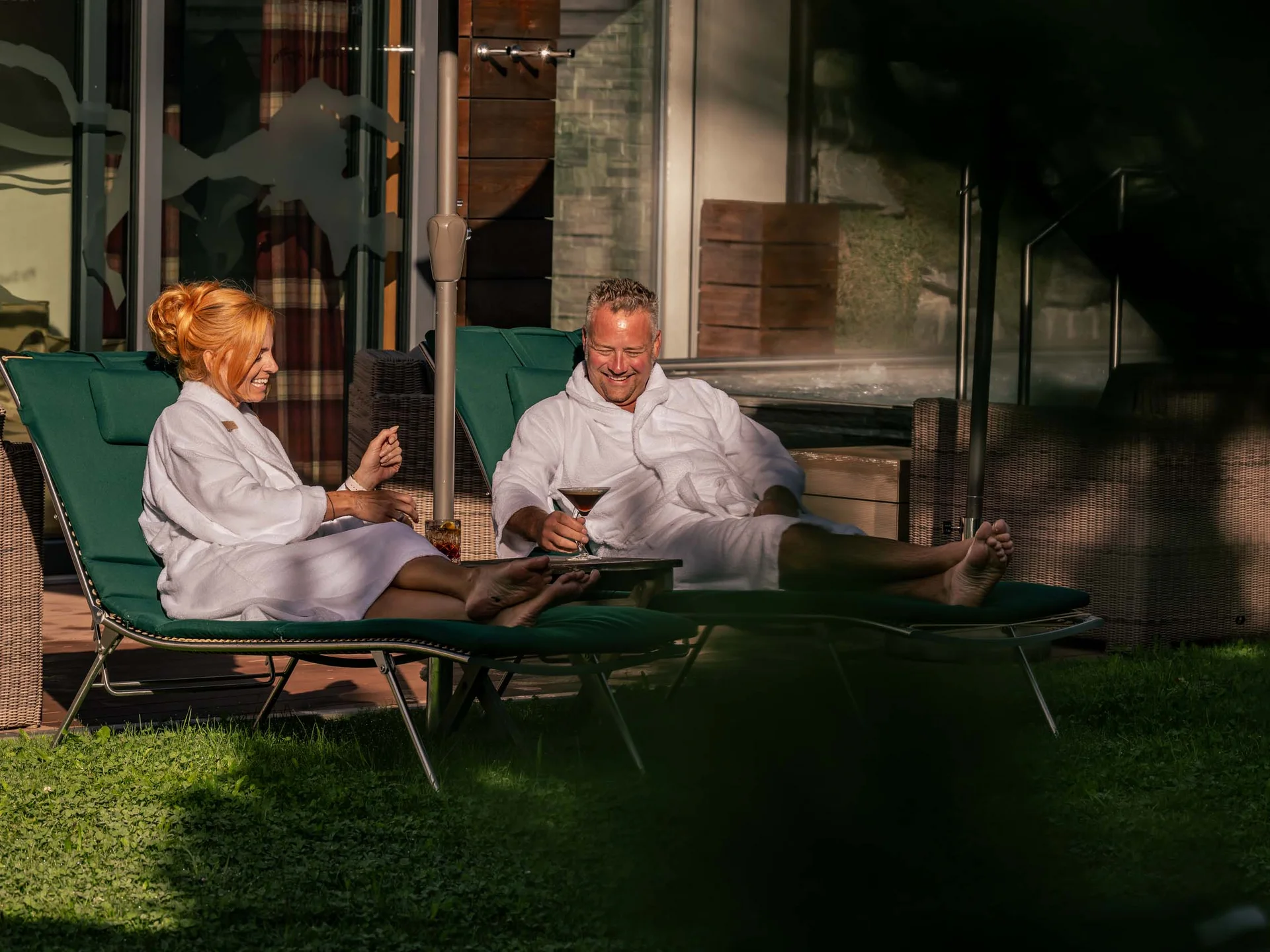 La Val Hotel & Spa: Ihr Hotel in Breil/Brigels Paar entspannt im Bademantel auf Liegestühlen mit Getränken im Freien